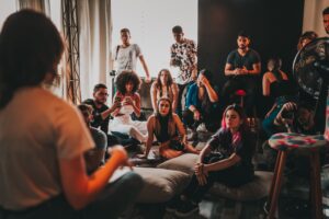 Group of attentive young multiracial community members in casual outfits meeting in modern studio and listening to female speaker sitting on mat